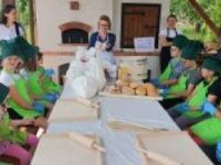 Zdjęcie przedstawia grupę uczestników, ubranych w ciemnozielone czapki i kucharskie i zielone fartuszki. Na stołach:...